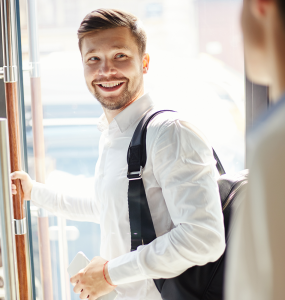 offboarding pracownika uśmiechnięty mężczyzna w białej koszuli otwiera szklane drzwi i patrzy się na innego mężczyznę