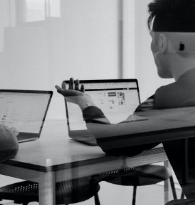 dwie osoby rozmawiające przy biurku i laptopach fotografia czarno-biała