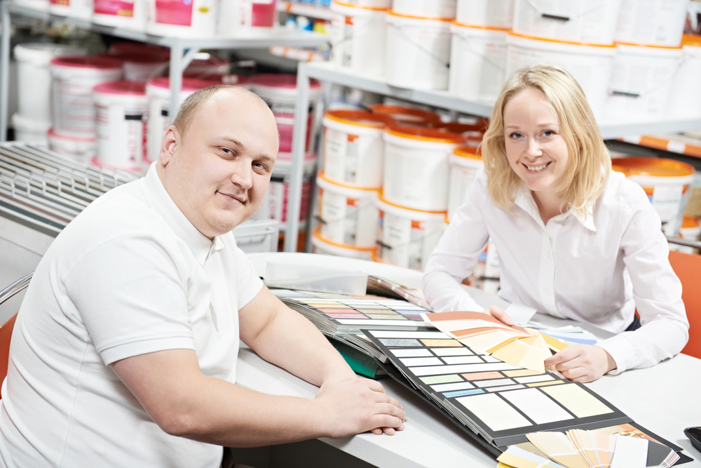 Man worker and woman client in a retail paint shop choose a color of a paint