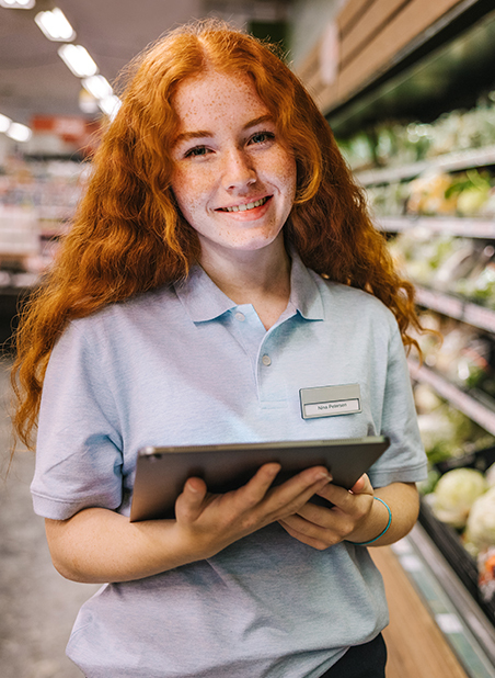 a young, ginger retail worker with a tablet in a store smiling